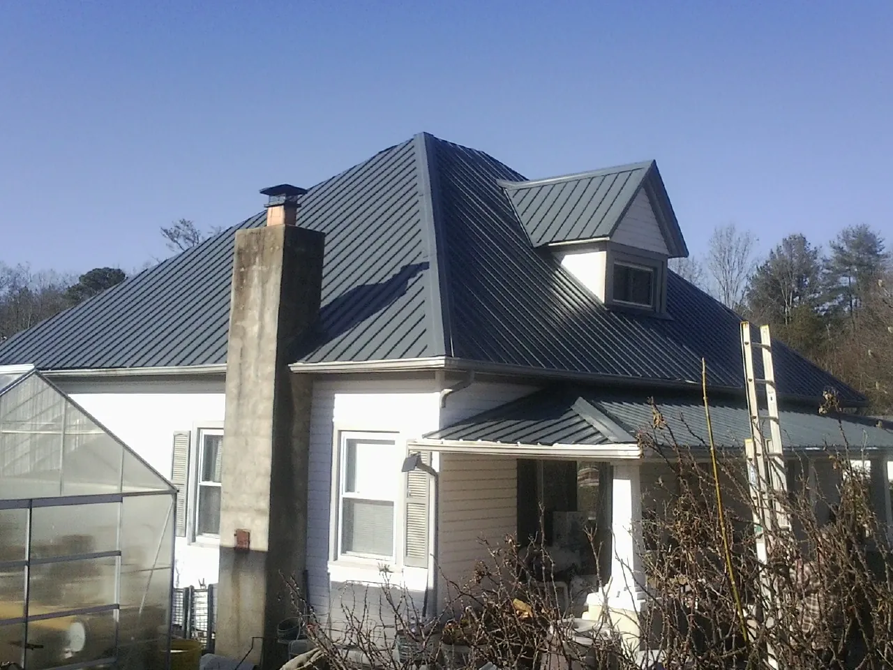 Dark blue standing seam metal roof on a white farmhouse with dormer — Slate & Tile Roof Repair by Roofing Brothers in Croghan