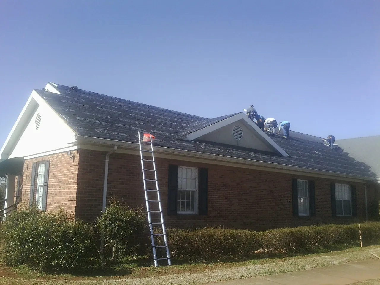 Crew tearing shingles off a brick ranch roof with a ladder set — Metal Roof Repair work by our crew in Croghan
