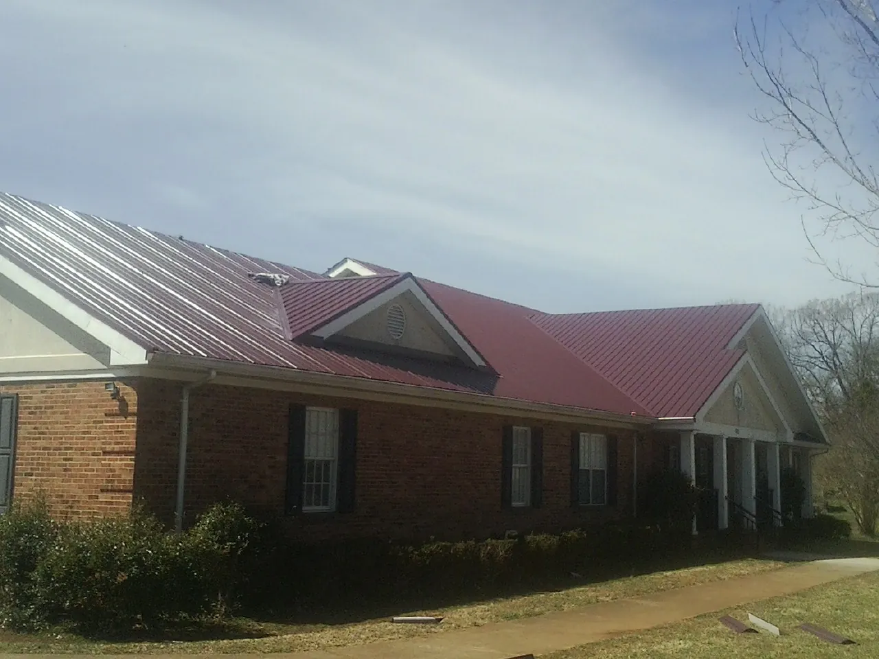 Red metal roof with gabled entries on a long brick building, from a Hail Damage Roof Repair job in Croghan