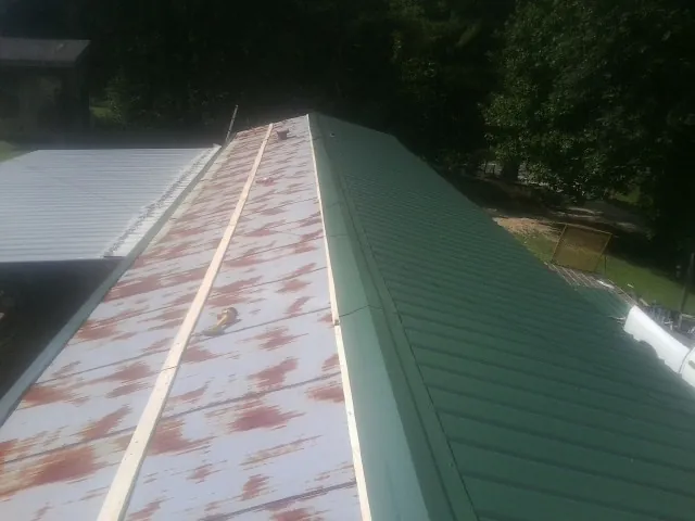 Old rusted panels beside newly installed green metal roofing — Wind Damage Roof Repair by Roofing Brothers in Croghan