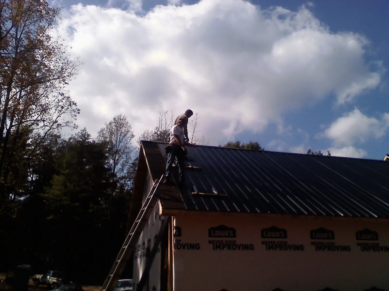 Roofer fastening dark metal panels high against a cloudy sky, from a Roof Inspection job in Croghan