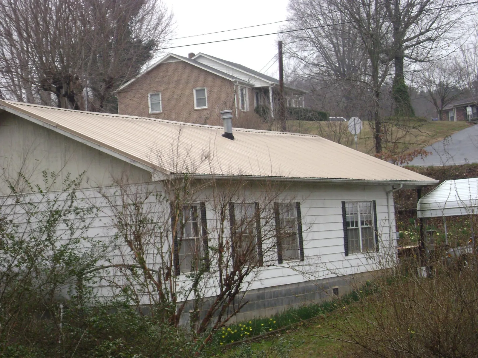 Tan metal roof on a white sided house set into a hillside — Commercial Roofing by Roofing Brothers in Croghan