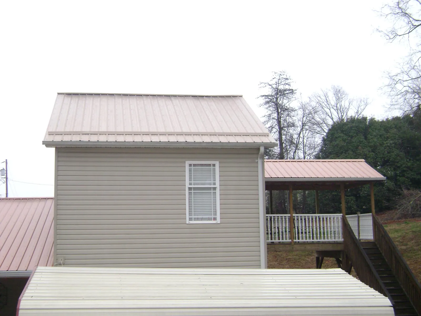 Tan metal roofs on a two story addition and attached porch, from a Roof Replacement job in Croghan
